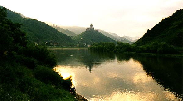 Bilden visar en borg på en spetsig kulle bortom en flodkrök, med runda kullar på båda sidor om floden.