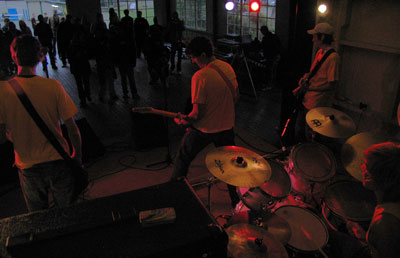 Bilden visar scenen, bakifrån sett, medan bandet spelar. Framför scenen syns publiken.