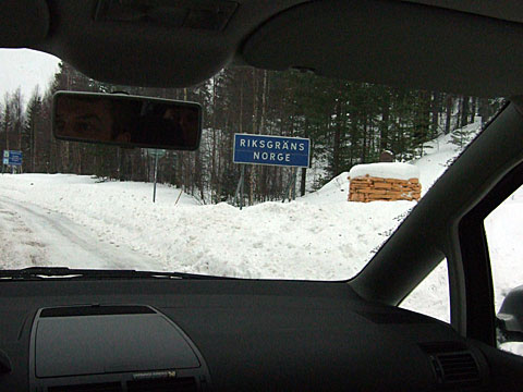 Bilden visar vintrig väg, inifrån bilen sett, när riksgränsens skylt passeras. 