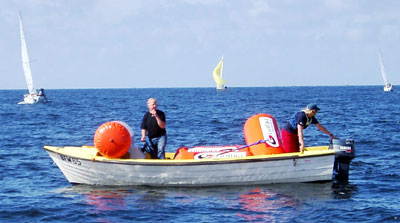Bilden visar två funktionärer i en stor styrpulpetbåt, som har rundningsbojar med sig.