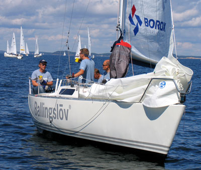 Bilden visar knoX i närbild, på öppet vatten med seglen nere. Besättningen fikar.