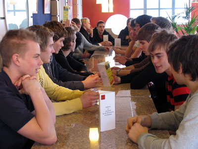 Bilden visar alla, som sitter runt ett avlångt bord och väntar på mat.