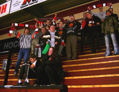 Bilden visar gänget på Gärdehovs ståplatsläktare. Många håller upp sin supporterhalsduk mellan utsträckta händer.
