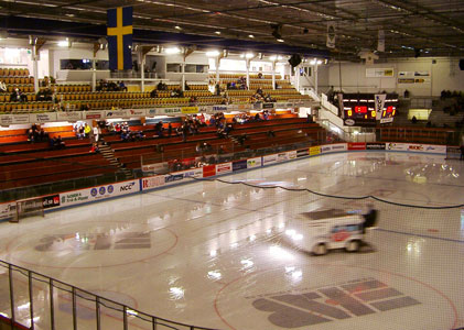 Bilden visar Björklövens hockeyhall inifrån, med dunkel belysning vid ena långsidans sittplatsläktare och en ismaskin som lyser upp lite på isen.