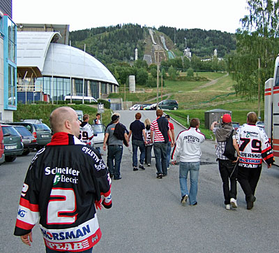 Bilden visar hockeysupportrarna, bakifrån sett, mellan bussen och arenan. I bakgrunden syns de två hoppbackarna.